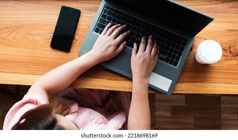 Top View Of Female Using Her Laptop On The Wooden Counter At A Cafe. Overhead Shot Of Young Woman Sitting At A Table With A Paper Coffee Cup 