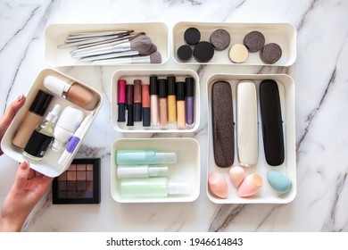 Top View Of Female Visagiste Is Neatly Placing Cosmetic And Vanity Items In MUJI's PP Makeup Storage Boxes With Various Sizes On White Marble Dressing Table. Decluttering And Organization Concept.