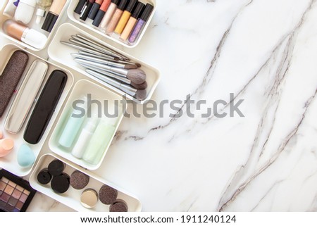 Top view of female visagiste is neatly placing cosmetic and vanity items in MUJI's PP makeup storage boxes with various sizes on white marble dressing table. Decluttering and organization concept.