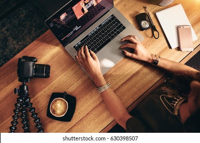 Top view of female vlogger editing video on laptop. Young woman working on computer with coffee and cameras on table. - Shutterstock ID 630398507