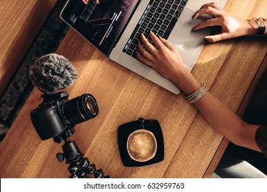 Top view of female vlogger editing video on laptop. Young woman working on computer with coffee and camera on table. - Powered by Shutterstock