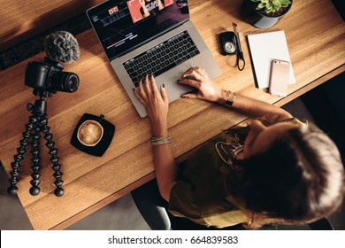 Top view of female vlogger editing video on laptop. Young woman working on computer with coffee and cameras on table. - Shutterstock ID 664839583