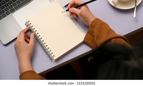 Top View, Female Writing On Her Diary In Creative Purple Office Desk. Woman Taking Notes On Spiral Notebook.