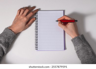 Top view of female's hand writing on a spiral notebook paper with red pencil - Powered by Shutterstock