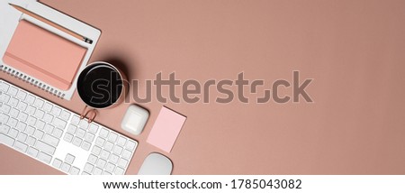 Top view of feminine workspace with computer keyboard, diary book, mug, accessories and copy space on pink table