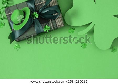 Top view of festive patrick composition on green background. Gift with satin green ribbon, hat, clover, perfect for St. Patrick's Day celebration. Flat lay