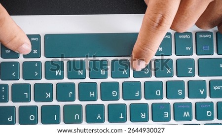 Top view of finger pressing command and C or cmd + C shortcut keys for copy on a green wireless computer keyboard isolated on black background