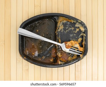 Top View Of A Finished Barbecue And Potato TV Dinner With A Fork In The Tray Atop A Wood Place Mat.