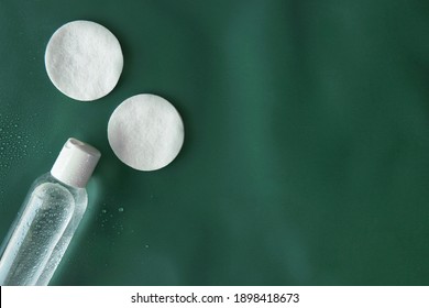 Top View First Step Routine Toner Facial Skincare Product Bottle With Round Organic Cotton Pad On Tidewater Green Solid Color Plain Background With Droplets And Copy Space