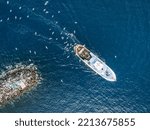 Top view of a fishing trawler coming back to the port and the seagulls are flying over it.