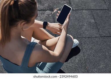 top view of fit woman in activewear with fitness tracker on wrist using smartphone after workout - Powered by Shutterstock