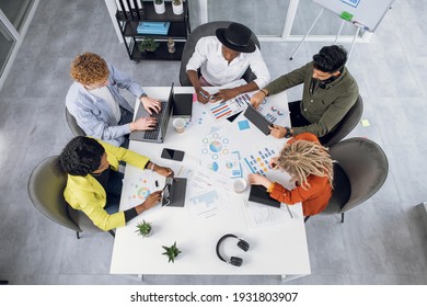 Top view of five international business people sitting together at office desk and working on personal gadgets. Creative young students using modern technology for work indoors.