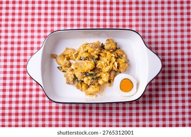Top view (flat lay) of authentic Indonesian lemon sauce chicken with salted egg, served in an oval white dish on a red checkered tablecloth