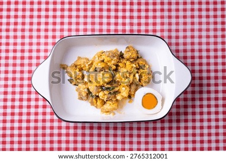 Top view (flat lay) of authentic Indonesian lemon sauce chicken with salted egg, served in an oval white dish on a red checkered tablecloth