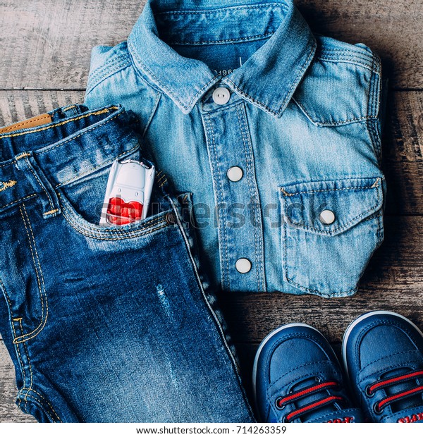 Top view, Flat Lay of Baby clothes blue jeans,\
sneakers, shirt and white baby kids car for game on wooden\
background. Top view