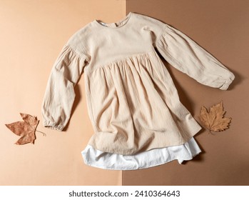 Top view flat lay beige children dress on beige and brown background.