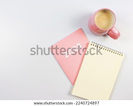 Top view or flat lay of blank paper note book on pink diary 2023 and pink cup of coffee on white background.
