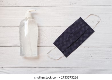 Top view or flat lay of blue washable and reusable cloth face mask and bottle of hand sanitizer gel for protection from spreading of coronavirus or COVID-19 , on white wooden background, minimal style - Powered by Shutterstock