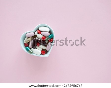 Top view, flat lay of blue heart-shaped bowl filled with a colorful assortment of various supplements on a pink wooden background, health, wellness, and care pharmacology concept.