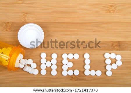 Top view flat lay bottle of pain pills spilled on wood table spelling the word HELP. Addiction and opioid epidemic theme imager with copy space.