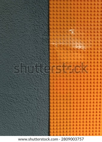 Top view or flat lay of bright orange plastic building blocks baseplate arranged next to a textured dark grey fabric or carpet background, creating a minimalist contrast.