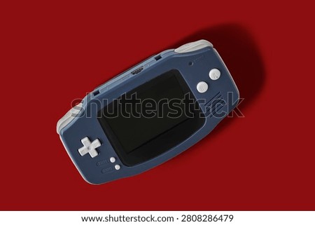 Top view flat lay of a classic dark blue portable handheld video game console on isolated red background. Retro equipment.