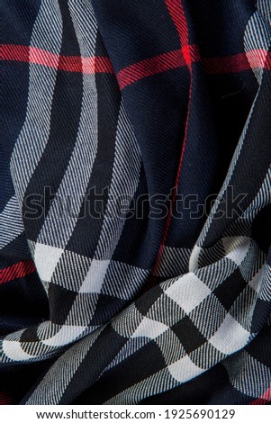 top view flat lay closeup part of folded dark blue checked scarf with white, black, and red strips