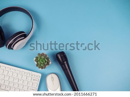 Top view or flat lay of computer keyboard  mouse, headphones, microphone and cactus on blue background with copy space. Online learning, online teaching, podcast background.