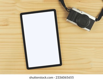 Top view or flat lay of digital tablet with blank white screen and digital camera isolated on wooden table background.