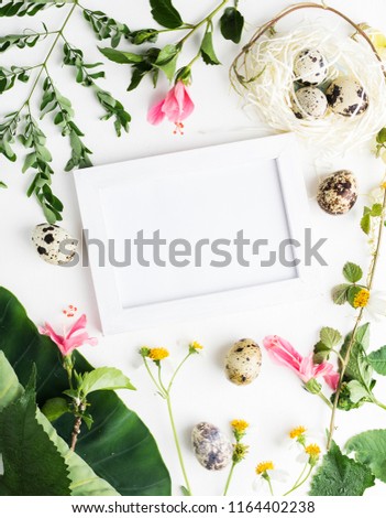 Top view flat lay Easter mockup: white photo frme with quail eggs, daisy flowers and green leaves. Holiday concept. Text space
