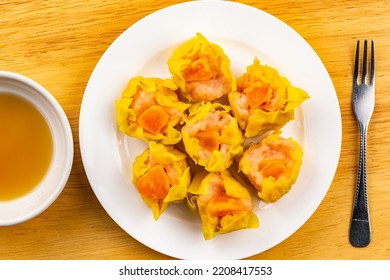 Top View, Flat Lay Fresh Delicious Homemade Shrimp, Minced Pork And Salted Egg Yolk Steamed Dumplings In White Ceramic Dish With Sauce In White Ceramic Cup And Metal Fork On Wooden Table.