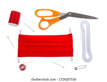 Top View Flat Lay Of Hand Make Surgical Style Face Mask With Bright Red Cotton Fabric. Supplies Elastic, Thread, Bobbin, Pins, Scissors And Safety Pin To Thread Elastic.