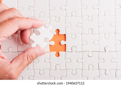 Top view flat lay of hand-holding last piece white paper jigsaw puzzle game last pieces put to place for solve problem complete mission, studio shot on an orange background, quiz calculation concept - Powered by Shutterstock