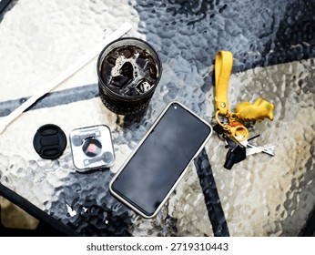 Top view flat lay of iced black coffee on a textured glass table with everyday personal items