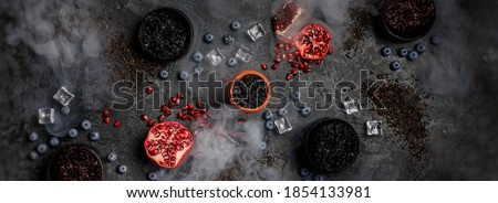 Top view or flat lay image of hookah tobacco. Hookah ceramic head fulled with aromated molose, pomegranade, blueberry and ice cubes on the grunge black table with smoke.