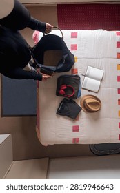 Top view flat lay of a man packing a travel bag on a bed with clothes, headphones, and a hat