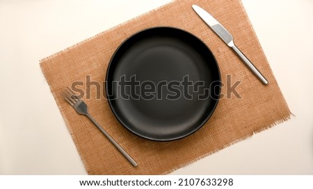 Top view, flat lay, a minimal dining table setting with empty black plate mockup and silverware over placemat.