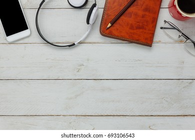 Top view / Flat Lay of the mobile phone and headphones on white rustic table with pen,diary also black coffee and eyeglasses background.An idea to relax time / rest or take a break with copy space.