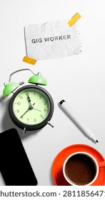 Top view flat lay of an office desk with a coffee cup, alarm clock, smartphone, and a note with the text 'Gig Worker' on a white background, symbolizing freelance and contract work