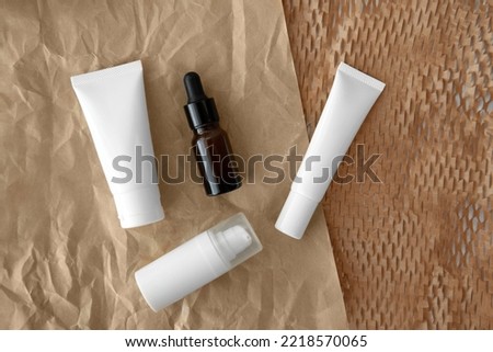 Top view or flat lay  packshot skincare facial white tube bottle blank label product glass serum with Ellwoods Gold Conifer green leaves on brown honeycomb wrap creased paper texture background