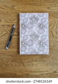 Top View Flat Lay of Patterned Hardcover Notebook And Black Pen On Wooden Surface with Copy Space