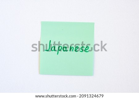 Top view flat lay of the reminder notepaper of green color with word Japanese on it on white background. Flashcards and language studies concept