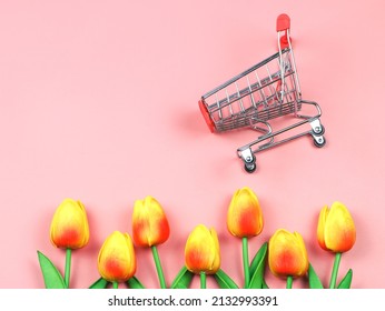 Top View Or Flat Lay Of Shopping Cart With Yellow Red Tulips On Pink Background. Spring Shopping Concept.