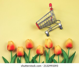 Top View Or Flat Lay Of Shopping Cart With Yellow Red Tulips On Yellow Background. Spring Shopping Concept.