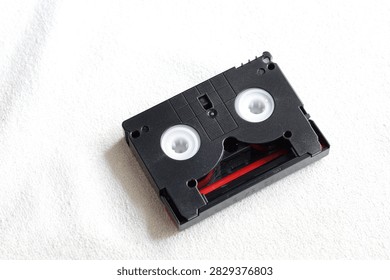 Top view flat lay of a single vintage MiniDV video cassette tape on white fabric background.