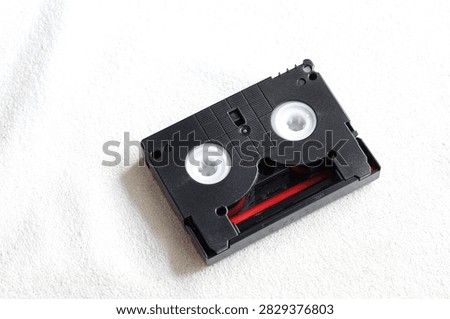 Top view flat lay of a single vintage MiniDV video cassette tape on white fabric background.
