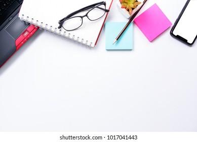 Top view or Flat lay style with copy space of workspace with laptop , pen , notebook , eyeglasses , sticky note and mobile phone on white table background or isolated