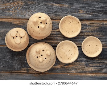 Top view flat lay of three handmade miniature speckled beige ceramic plant pots and matching saucers on dark wooden surface. Artisanal hand-built pottery showing functional drainage holes and organic stone-like texture. Minimalist clay craft for small succulents and modern home decor.