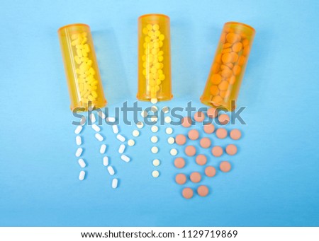 Top view flat lay three medication bottles spilling contents out onto blue background.