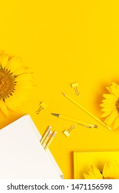 Top view flat lay of workspace desk styled design with sunflowers, white paper bag, pencils, pen, paper clips on bright yellow background. Autumn or summer Concept. Sunflower natural background. 